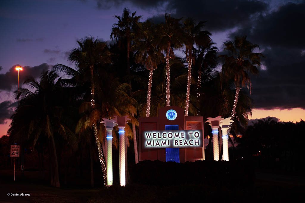 Illuminated Welcome to Miami Beach sign at night among lit palm trees